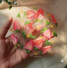 a hand is holding a glass plate with flowers on it and painted onto the surface