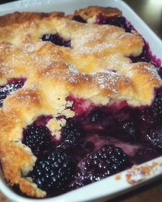 a close up of a pie in a pan on a table with blueberries and powdered sugar