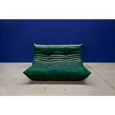 a green couch sitting on top of a cement floor next to a blue wall in an empty room