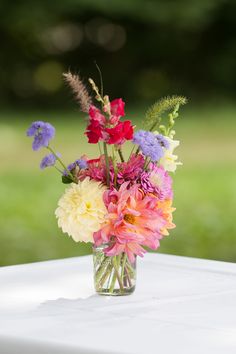 a glass vase filled with colorful flowers on top of a white tablecloth covered table