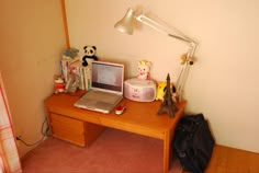 a laptop computer sitting on top of a wooden desk next to a lamp and stuffed animals