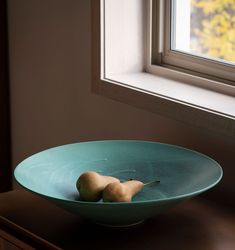 two pears sit in a bowl on a table next to a window sill