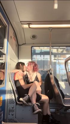 two women sitting on a bus with their backs to each other and one is kissing the other