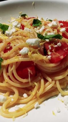 a white plate topped with spaghetti and tomatos on top of fettuccine