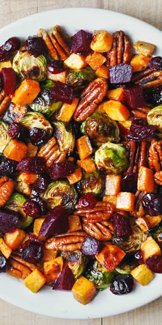 a white plate topped with roasted vegetables and pecans on top of a wooden table