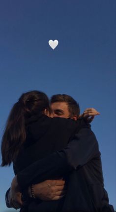 two people hugging each other with a heart shaped object in the sky