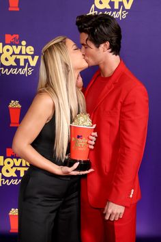 a man and woman kissing while holding popcorn in front of a purple wall with the words i love tv awards written on it