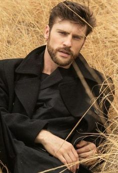 a man sitting in tall grass wearing a black coat