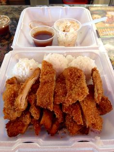 a plastic container filled with fried chicken and rice next to dipping sauce on a table