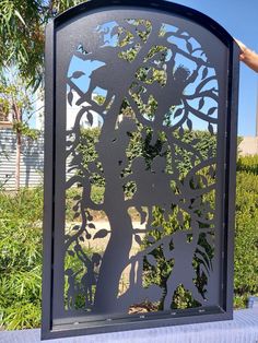 a person is holding up a metal screen with an image of a tree on it