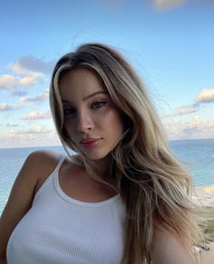 a beautiful young woman standing next to the ocean