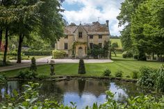 a large house sitting in the middle of a lush green field next to a pond