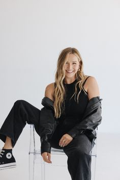 a woman sitting in a chair with her legs crossed, smiling and wearing black sneakers