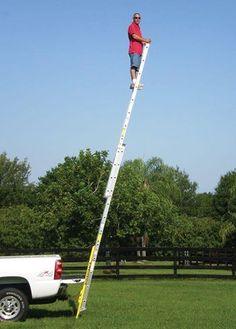 a man standing on top of a ladder next to a white truck in a field