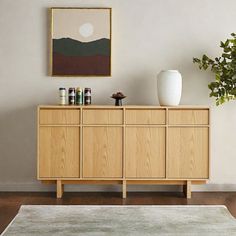 a living room with a large painting on the wall next to a wooden cabinet and rug