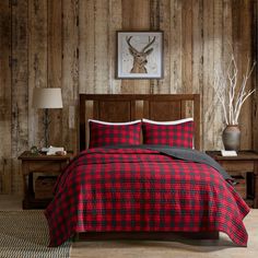 a bed with red and black plaid comforter in a rustic style bedroom, next to a wooden wall