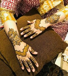 two hands with henna tattoos on them sitting next to pillows and flowers in the background