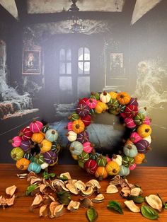 a wreath made out of colorful balls and leaves on a wooden table in front of a painting