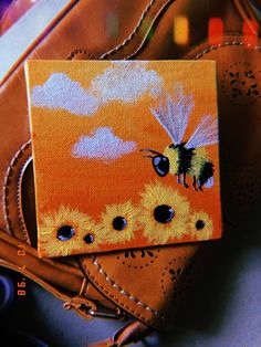 a painting of a bee on an orange and yellow background next to a brown purse