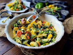 a bowl filled with corn and vegetables on top of a wooden table next to other dishes