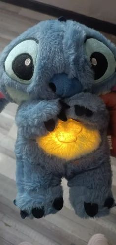 a blue stuffed animal with big eyes holding a yellow light in it's mouth