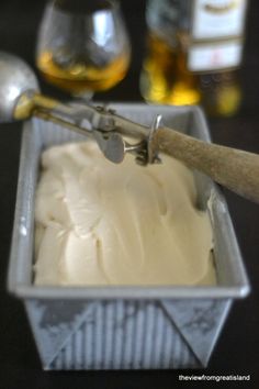 an ice cream in a metal container with a spoon and some liquor bottles behind it