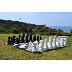 a giant chess set on top of a grass covered field next to the ocean and trees