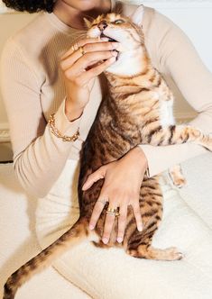 a woman holding a cat while sitting on top of a white couch next to a wall