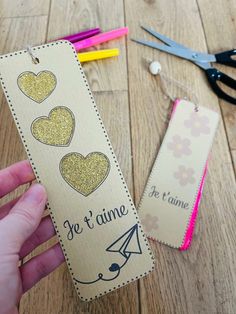 a person holding up a bookmark with scissors next to it on a wooden floor