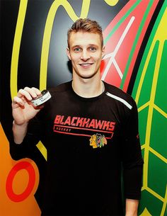 a young man holding a cell phone in his right hand and wearing a black hawks t - shirt