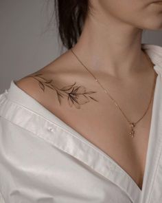 a woman with a tattoo on her chest is wearing a white shirt and gold necklace