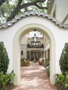 an archway leads to the front entrance of a large white house with trees and shrubs around it