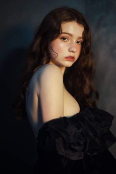 a woman with long hair wearing a black dress and posing for a photo in front of a dark background