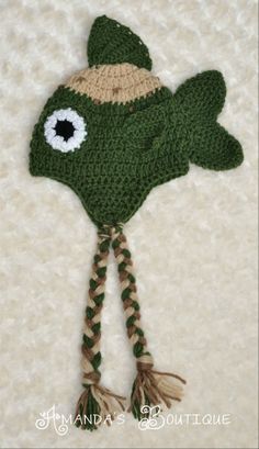 a crocheted green hat with white eyes and braids on the bottom, attached to a hook