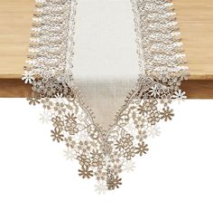 an embroidered table runner with white flowers and lace on the edge, hanging from a wooden table