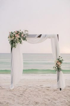 an outdoor wedding setup on the beach with white draping and pink flowers at the top