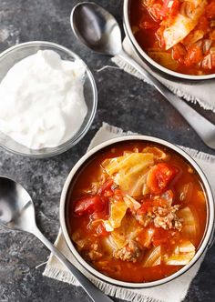 two bowls of cabbage soup with sour cream and spoons next to them on a table