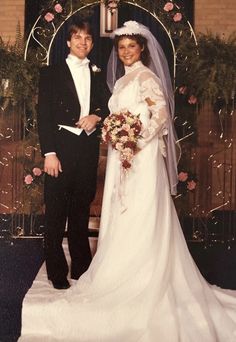 a bride and groom posing for a photo in front of an arch decorated with flowers