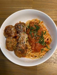 a white bowl filled with spaghetti and meatballs on top of a wooden table next to a fork