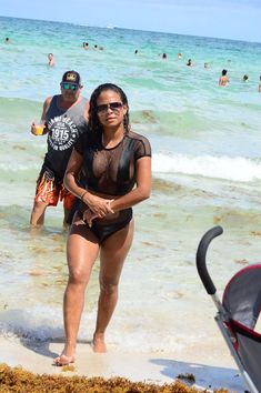 a woman in a black bodysuit walking into the ocean with two men behind her