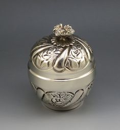 an ornate silver box with a flower on the top is sitting on a gray surface