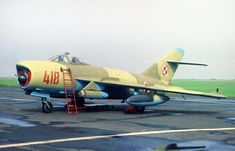 a fighter jet sitting on top of an airport tarmac next to a man in a ladder