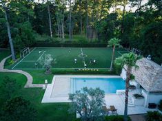 an aerial view of a tennis court and pool in the middle of a lush green yard