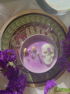 two skulls are sitting in a bowl with purple flowers around it on a table top