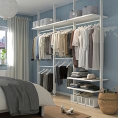 a bedroom with blue walls and white shelving, clothes on hangers in front of the bed