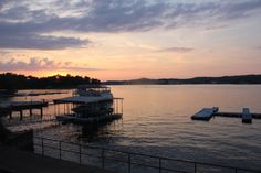 boats are docked at the end of a pier as the sun sets