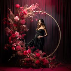 a pregnant woman standing in front of a circular frame with flowers and branches on it