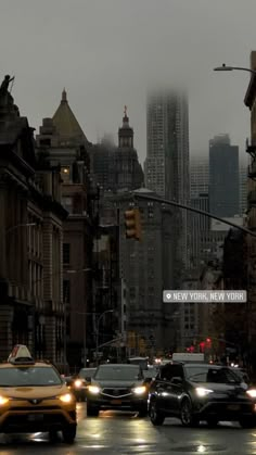 cars driving down the street in front of tall buildings and skyscrapers on a rainy day