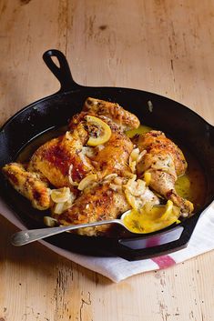 a skillet filled with chicken and vegetables on top of a wooden table next to a fork