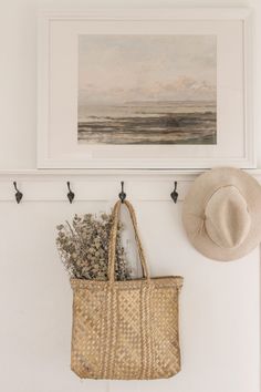 a basket and hat are hanging on the wall next to a framed painting with an ocean scene